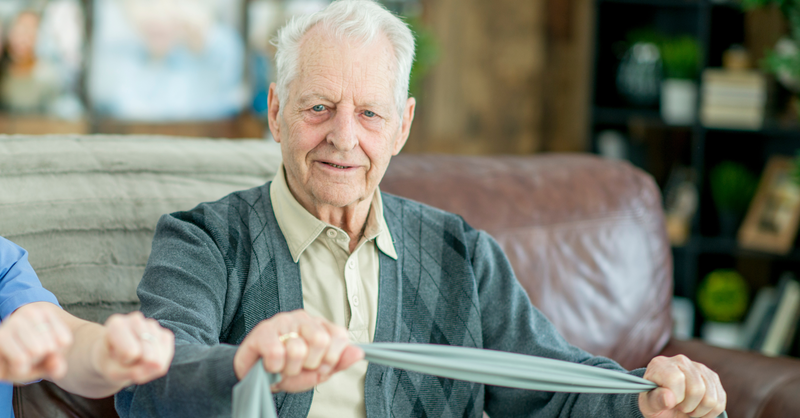 Elderly man using resistance band for rehabilitation exercises at home